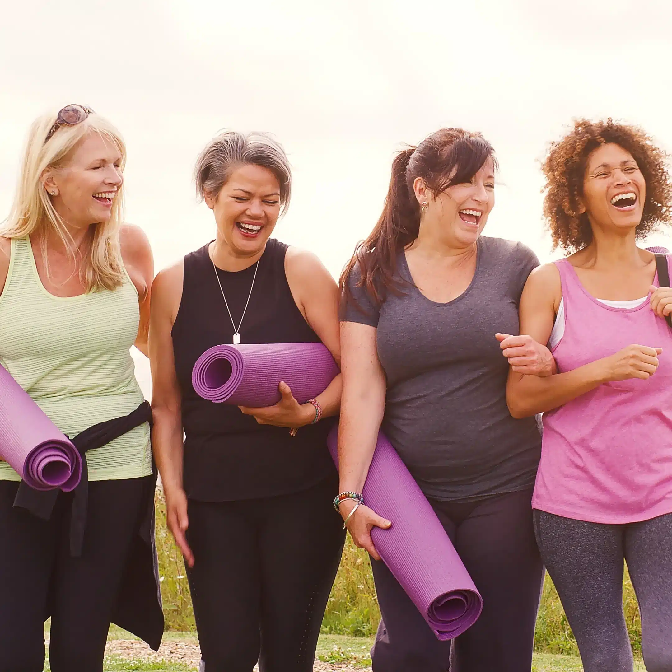 Four women laughing together outdoors with yoga mats – friendly yoga classes and community at Embrace Wellness Newbury Berkshire Small group yoga and meditation class in Newbury with Embrace Wellness — mindfulness yoga classes in Newbury led by Manlee