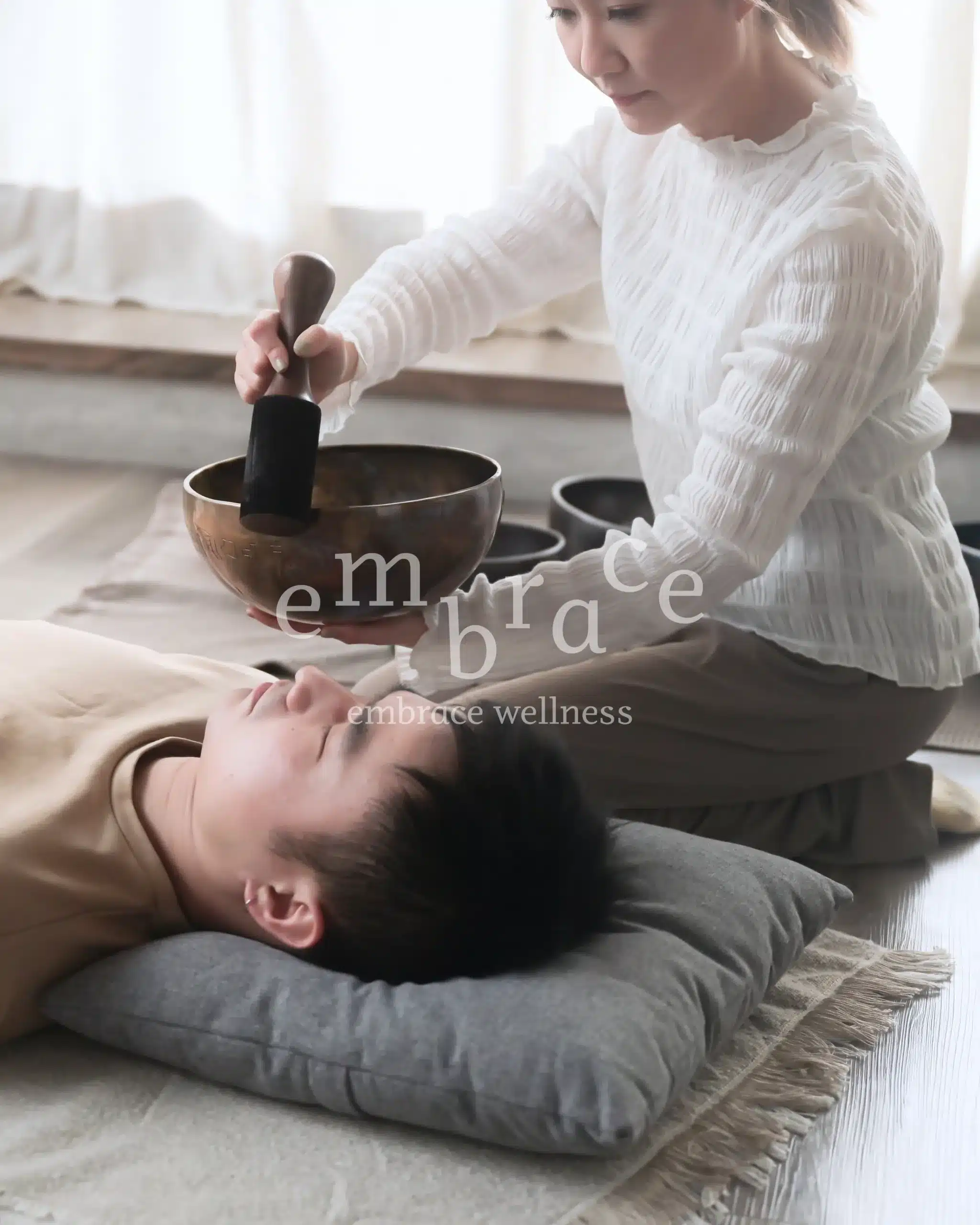 Manlee W playing a Tibetan singing bowl over a resting client – private sound bath session at Embrace Wellness Newbury