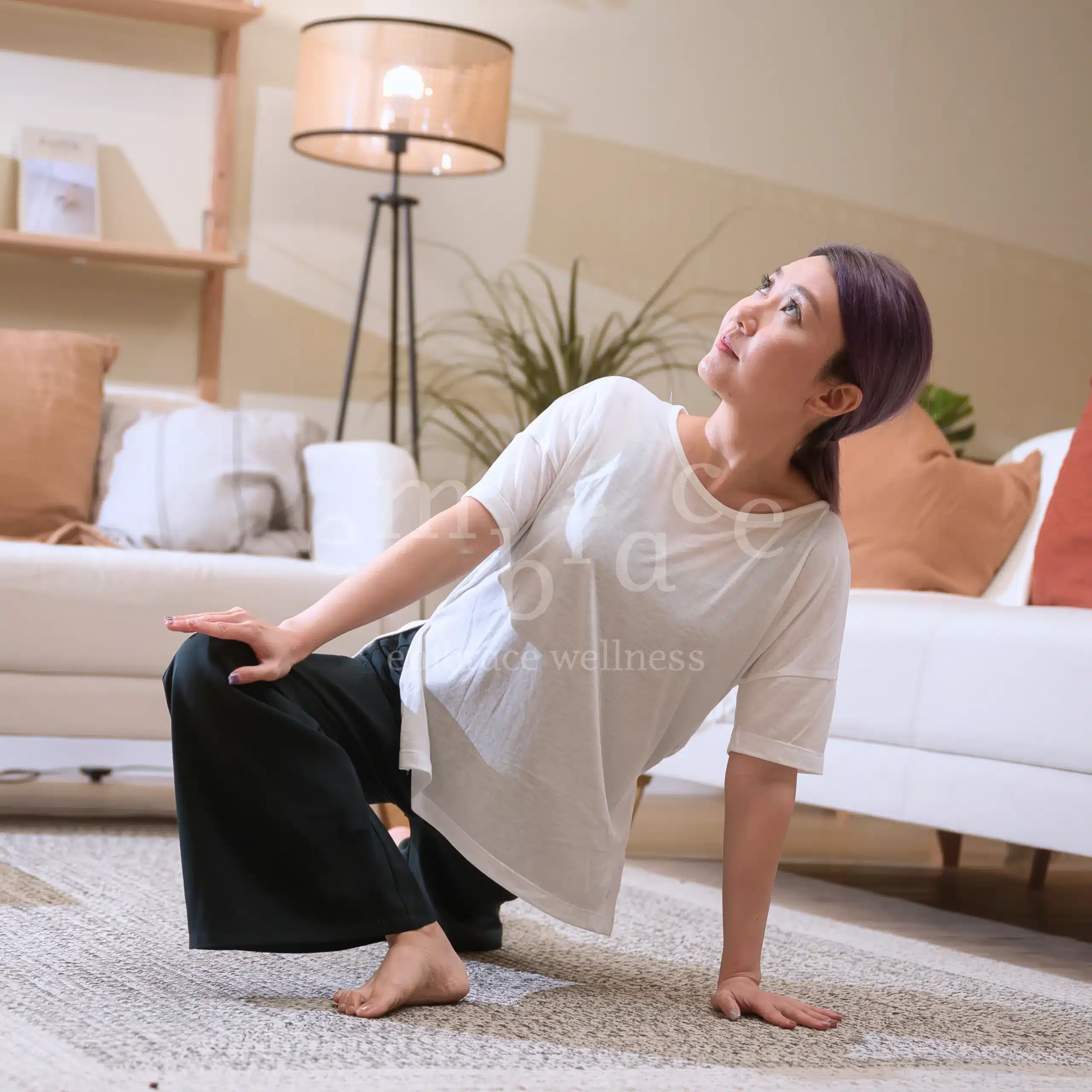 Manlee W, a yoga teacher from Newbury Berkshire, seated in a gentle twisting pose, showing a blend of mindful movement and stillness in a warm, calming studio setting.
