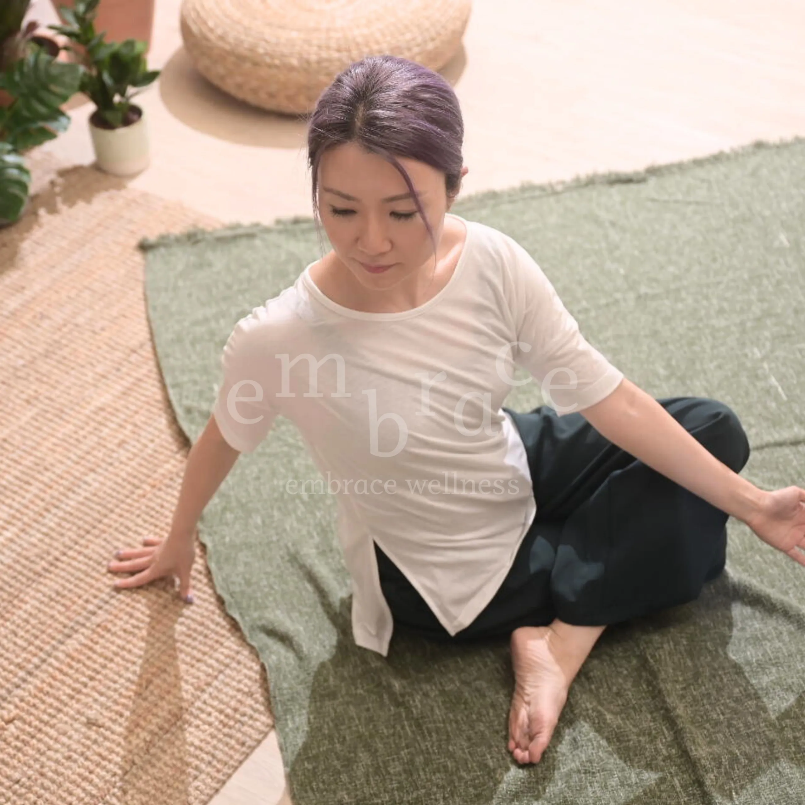 Manlee W, a yoga teacher from Newbury, seated in a gentle twisting pose, showing a blend of mindful movement and stillness in a warm, calming studio setting.