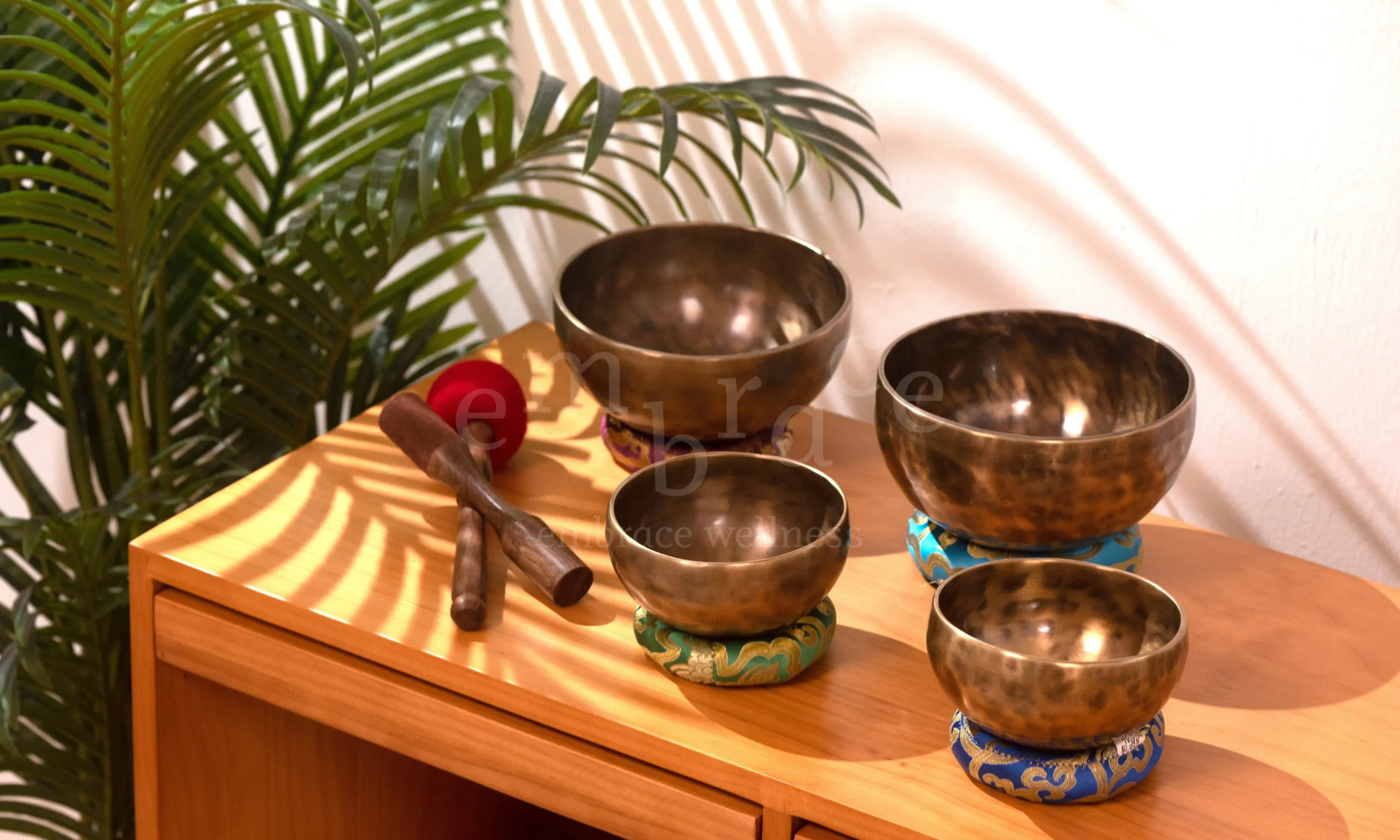 Handcrafted Tibetan singing bowls on a wooden table with mallets, symbolising authentic sound healing and mindfulness craftsmanship.