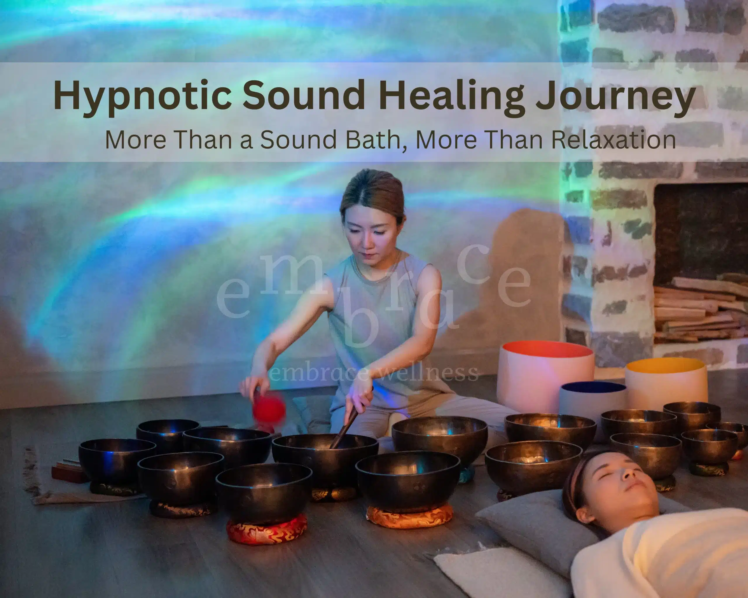 Certified sound healer Manlee playing crystal singing bowls and Tibetan singing bowls during a private Hypnotic Sound Healing Journey session at Embrace Wellness, with a client lying peacefully surrounded by crystal and Tibetan bowls under atmospheric coloured light. Sound bath in Newbury, Berkshire