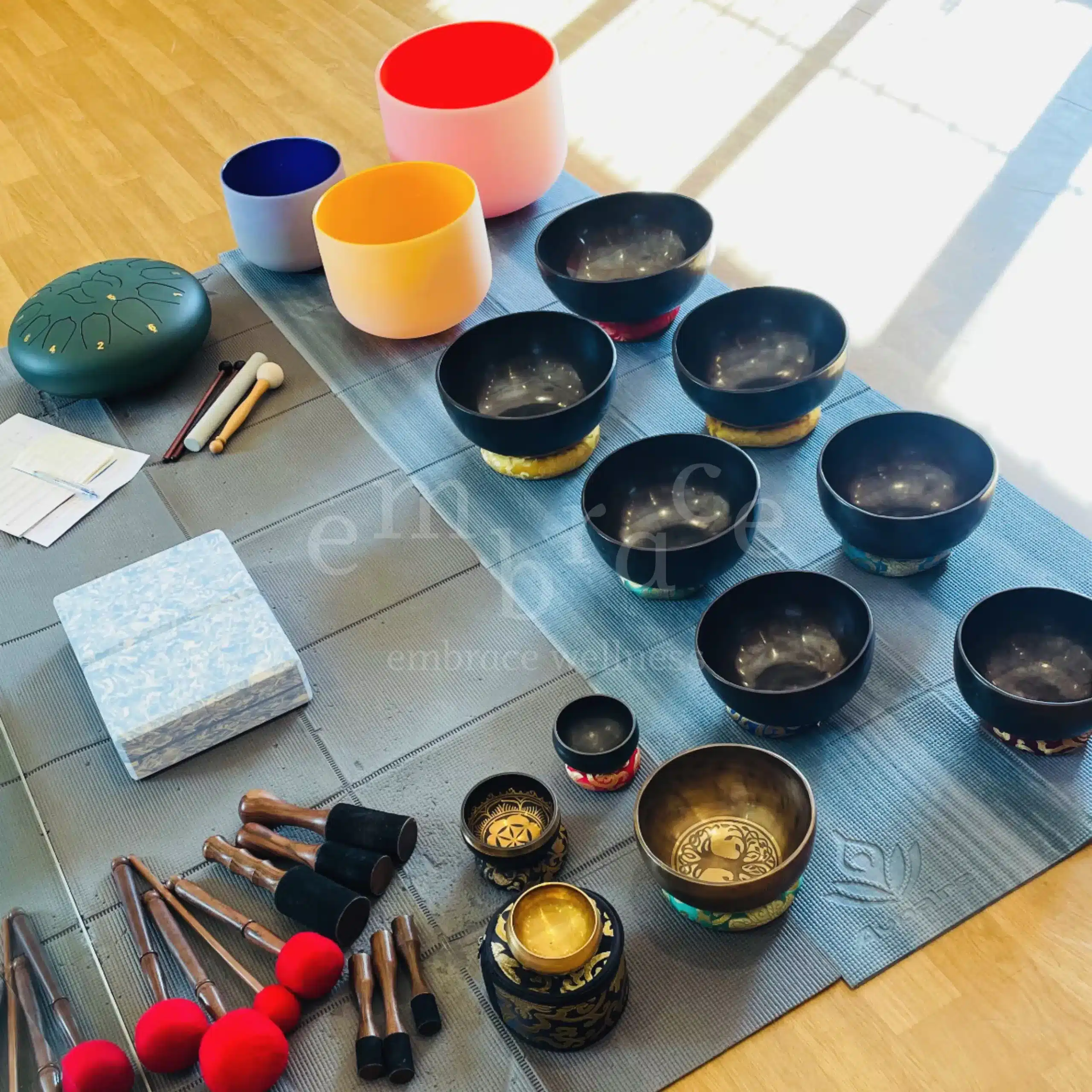 A collection of carefully selected Tibetan singing bowls, crystal singing bowls, a tongue drum, and mallets laid out on a mat — sound healing instruments used in Hypnotic Sound Healing Journey sessions at Embrace Wellness, Newbury, Berkshire