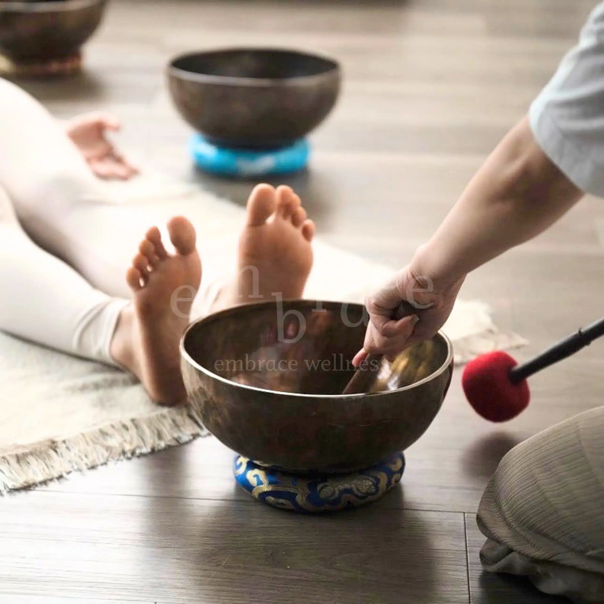 Close-up of a large antique Tibetan singing bowl on a blue embroidered cushion at the feet of a relaxed client during a sound healing session at Embrace Wellness Newbury with sound healer Manlee W